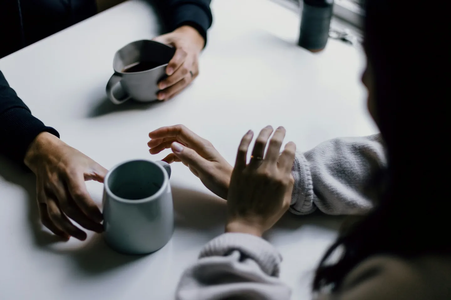 Zwei Menschen im Gespräch an einem hellen Tisch, zu sehen sind ihre Hände und Tassen